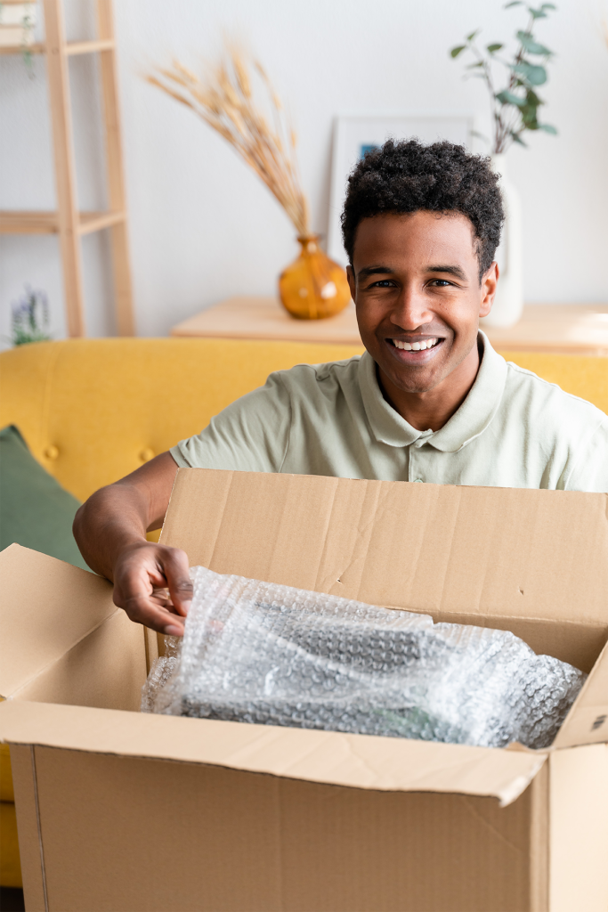 Smiling man unboxing a package filled with bubble wrap at home.
