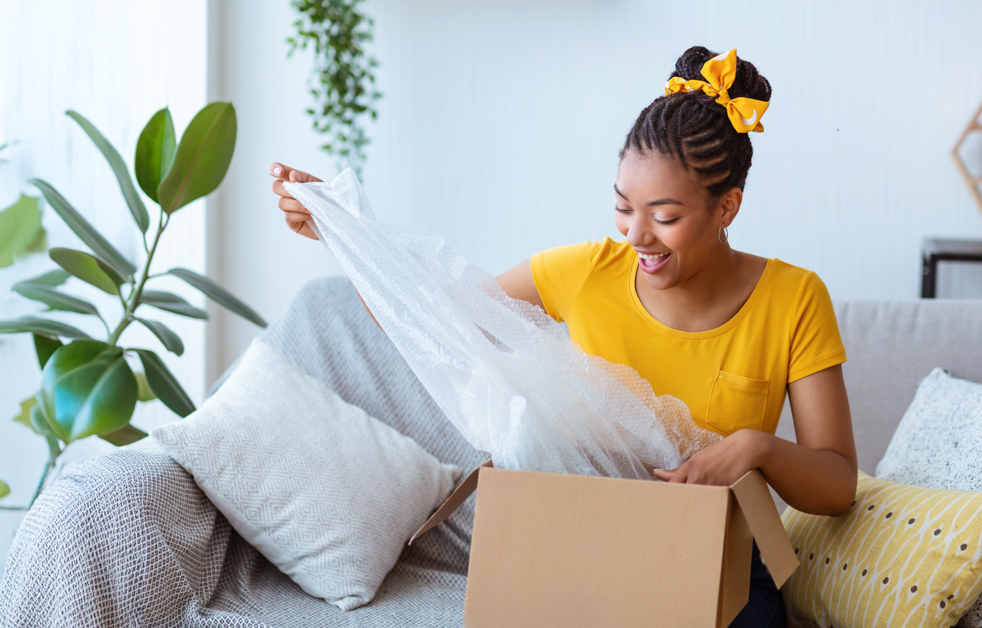 Happy woman unboxing a package on her couch after online shopping, smiling and excited to see the contents.